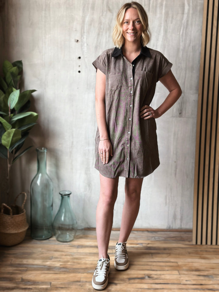Woman wearing a brown dress standing in a room with a plant and decorative bottles.