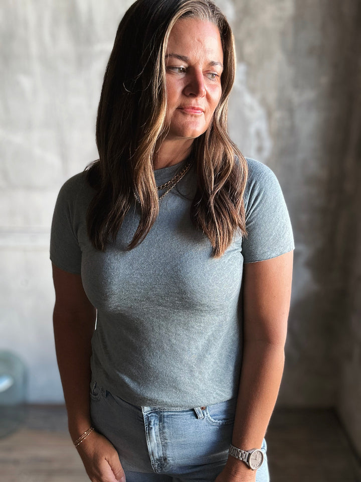Woman wearing a gray t-shirt and jeans standing against a textured wall.