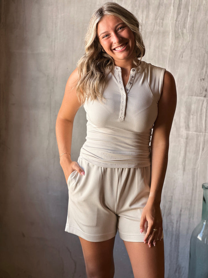 Woman wearing a white sleeveless top and shorts against a neutral background