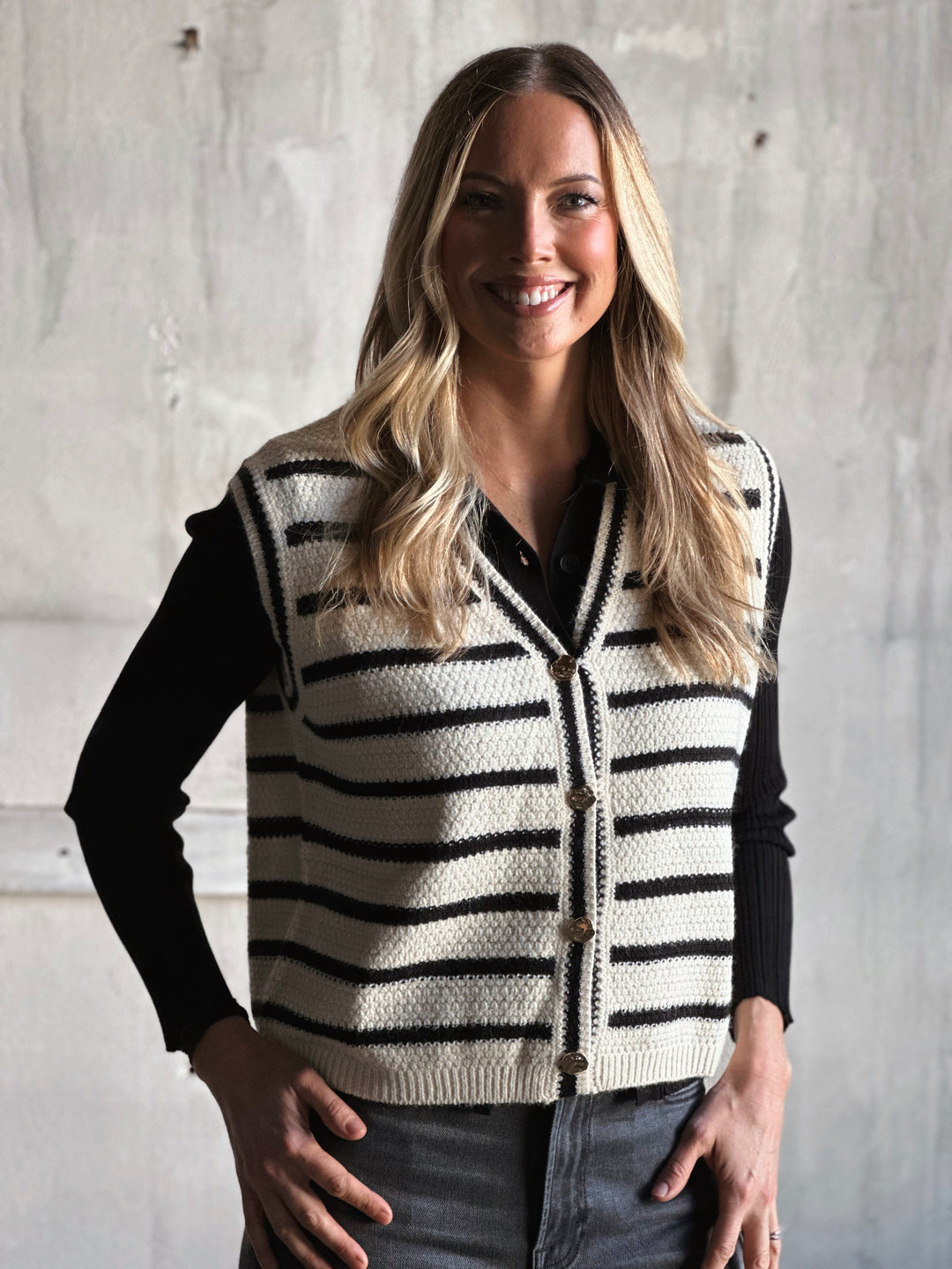 Woman wearing a black and white striped vest against a concrete wall.
