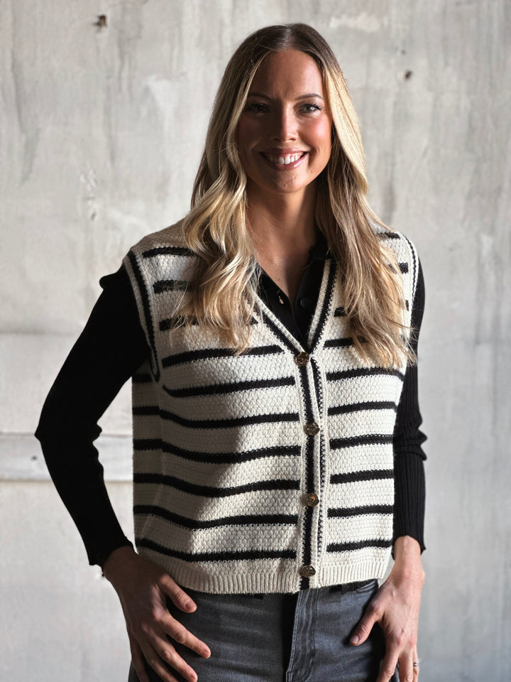 Woman wearing a black and white striped vest against a concrete wall.
