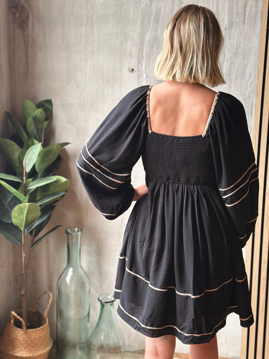 Woman wearing a black dress with white trim standing in front of a textured wall.
