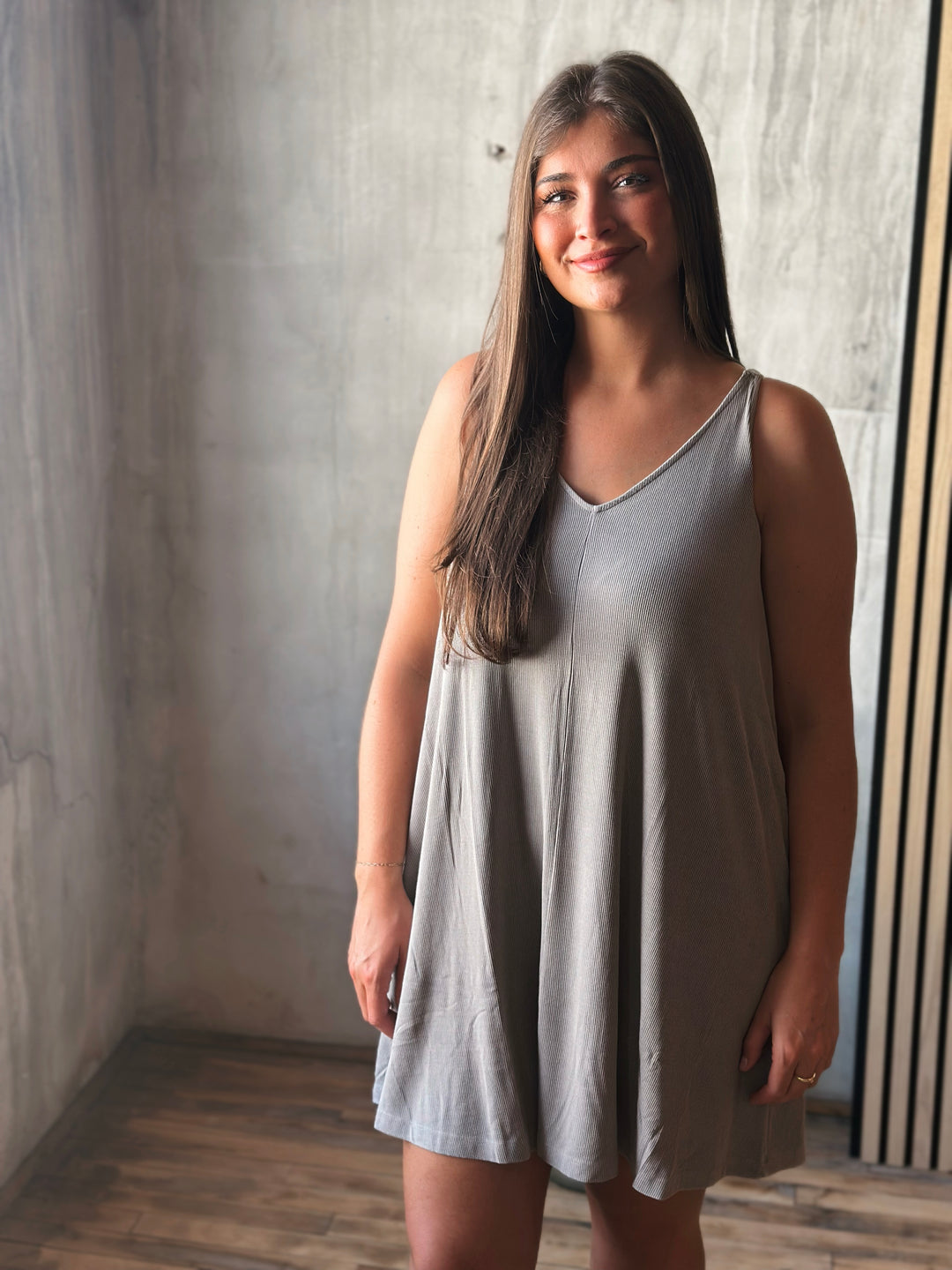 Woman wearing a light gray sleeveless dress standing against a textured wall.