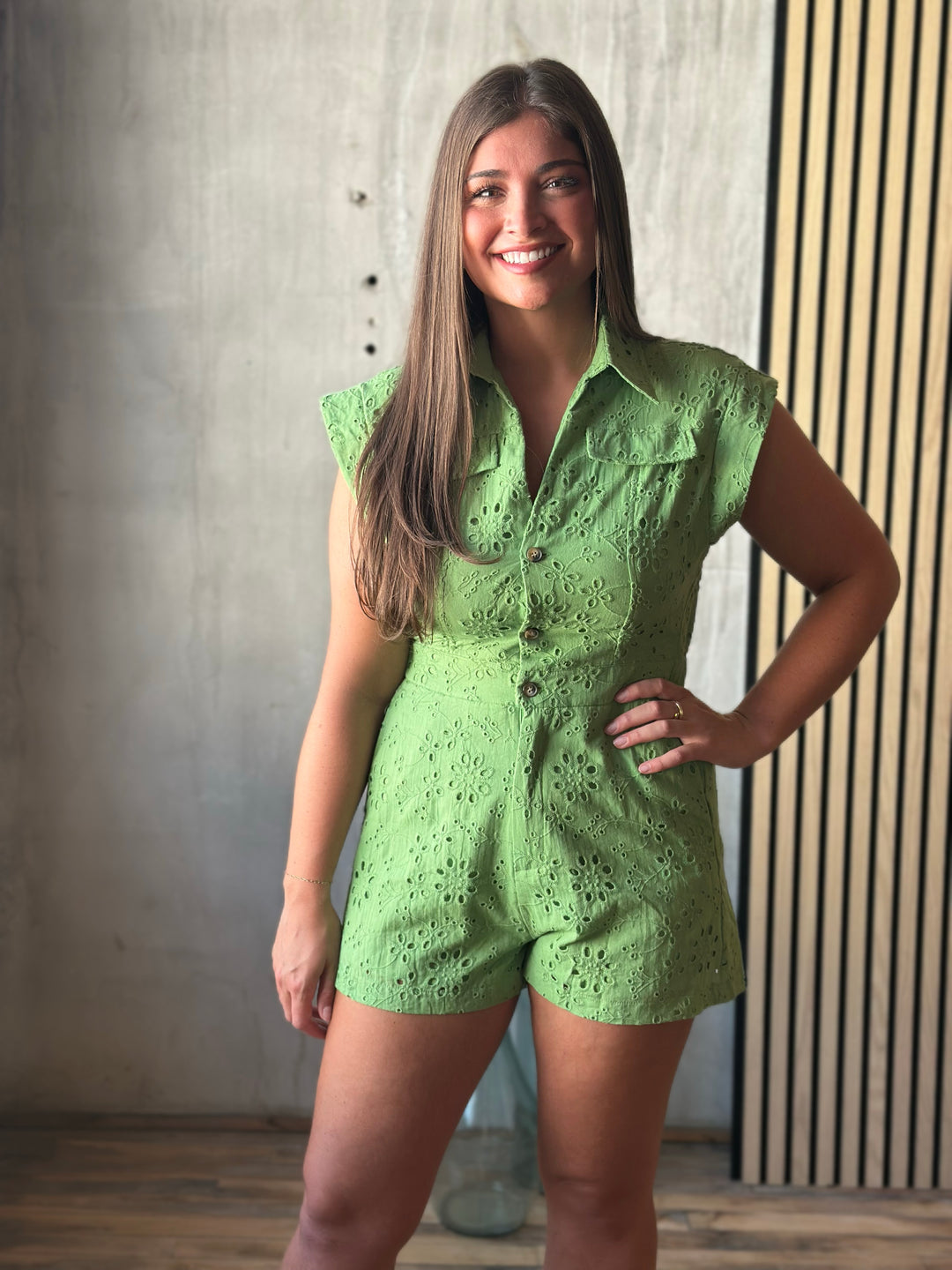 Woman wearing a green lace romper standing against a textured wall.