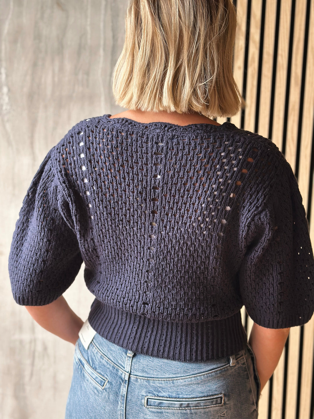 Person wearing a dark blue knitted sweater with a textured pattern, standing against a neutral background.