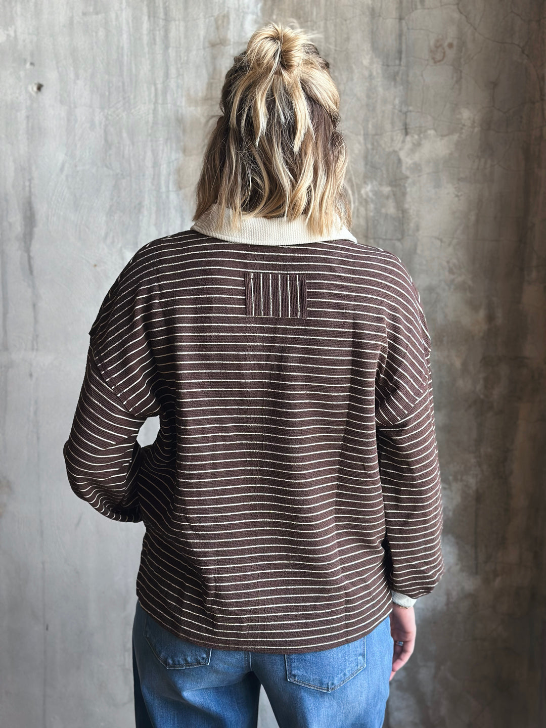 Person wearing a brown striped shirt against a gray concrete wall