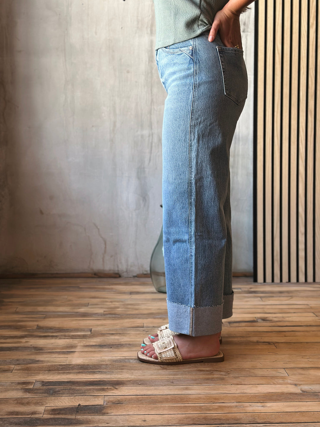 Person wearing light blue jeans standing on a wooden floor with a neutral wall background