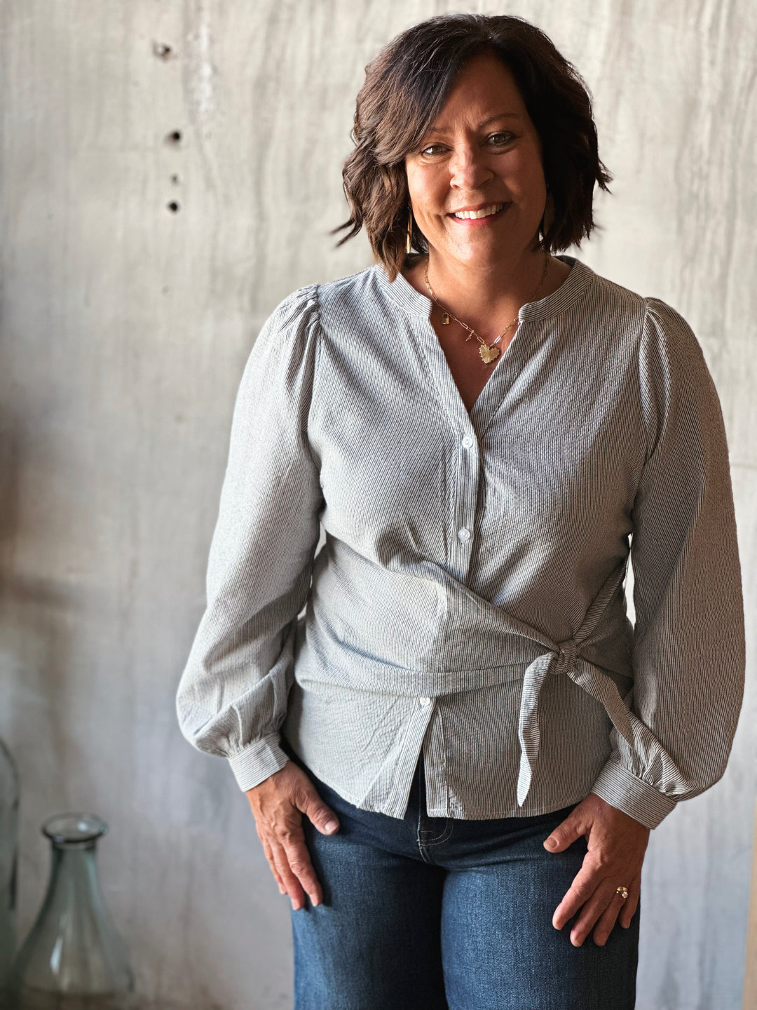 Woman wearing a light gray blouse with a tie detail in front of a neutral background