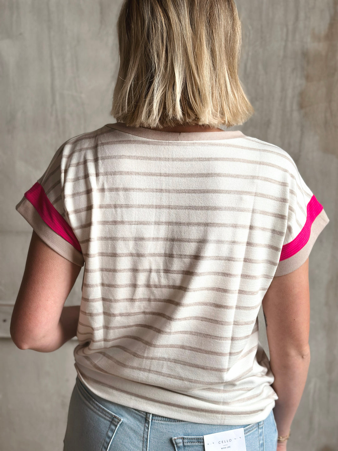 Person wearing a striped shirt with pink accents against a plain background