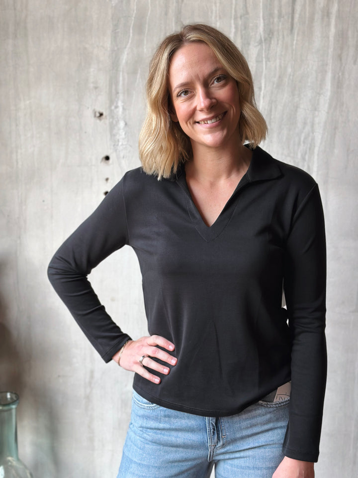 Woman wearing a black long-sleeve shirt and blue jeans against a neutral background