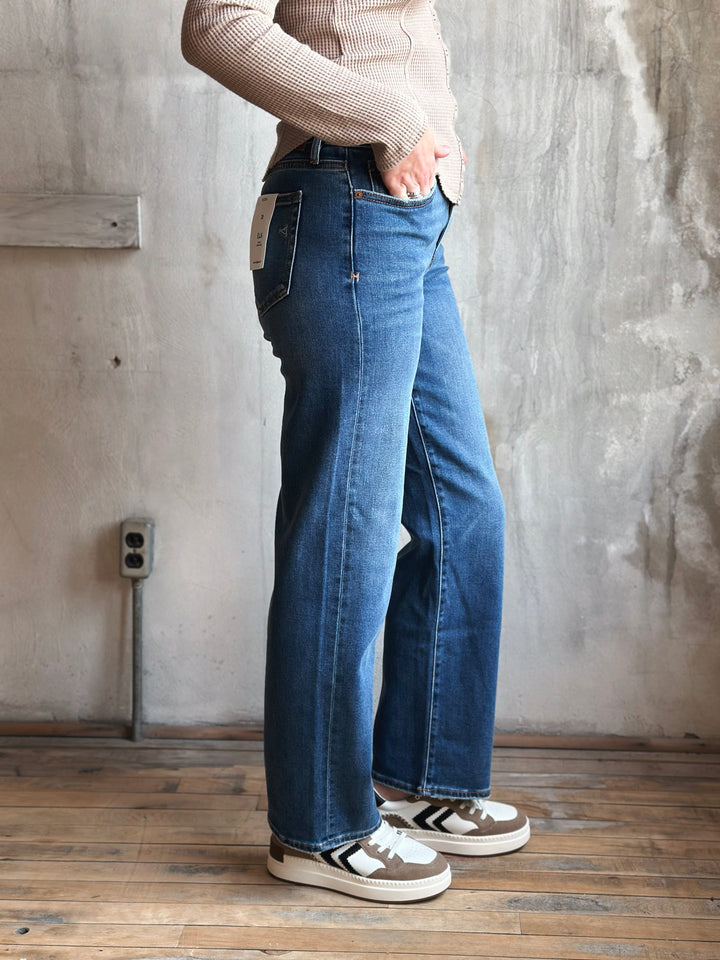 Person wearing blue jeans and a beige sweater in a room with a concrete wall.