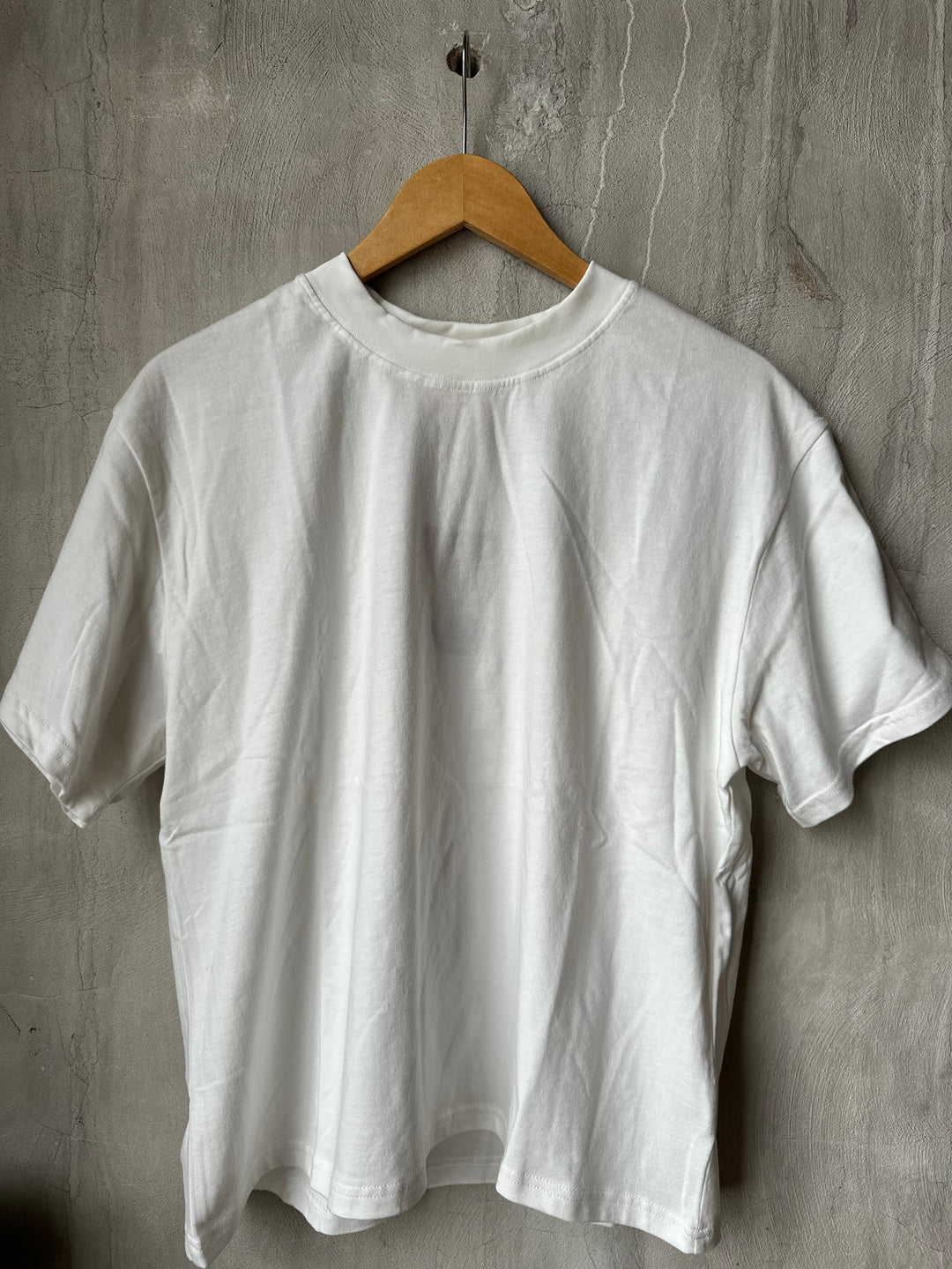 White t-shirt on a wooden hanger against a gray concrete wall