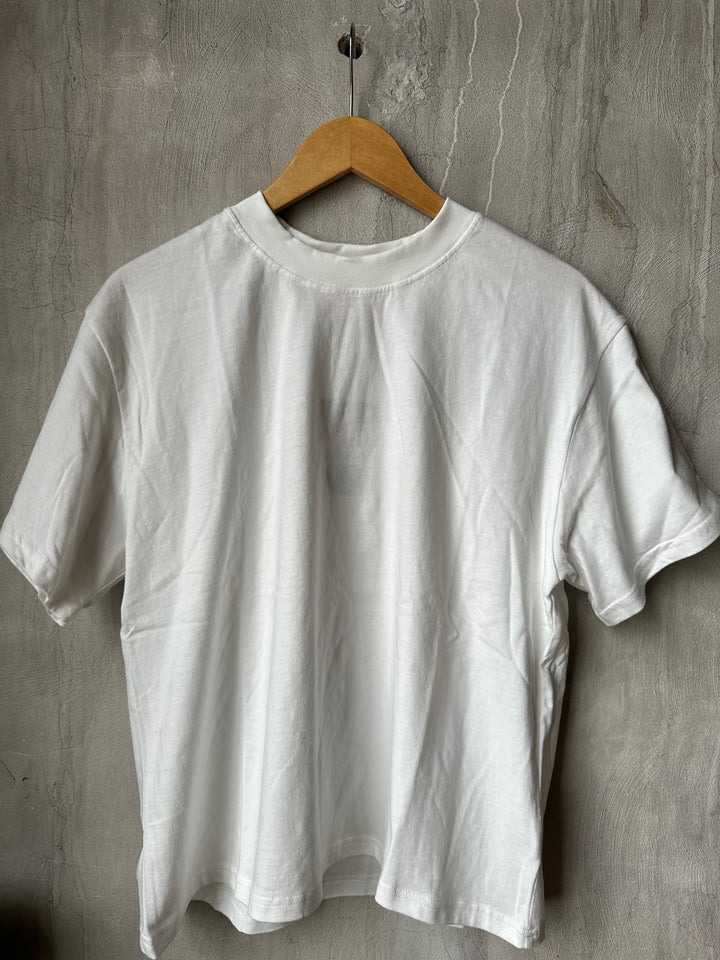White t-shirt on a wooden hanger against a gray concrete wall