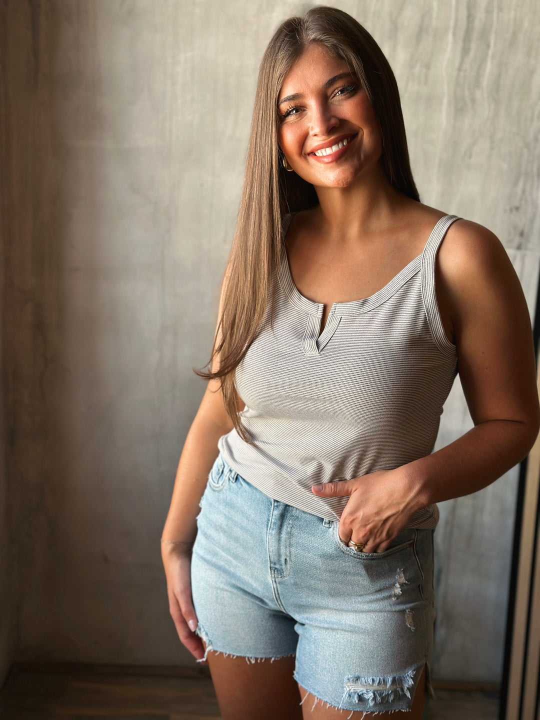 Woman wearing a light gray tank top and denim shorts against a neutral background