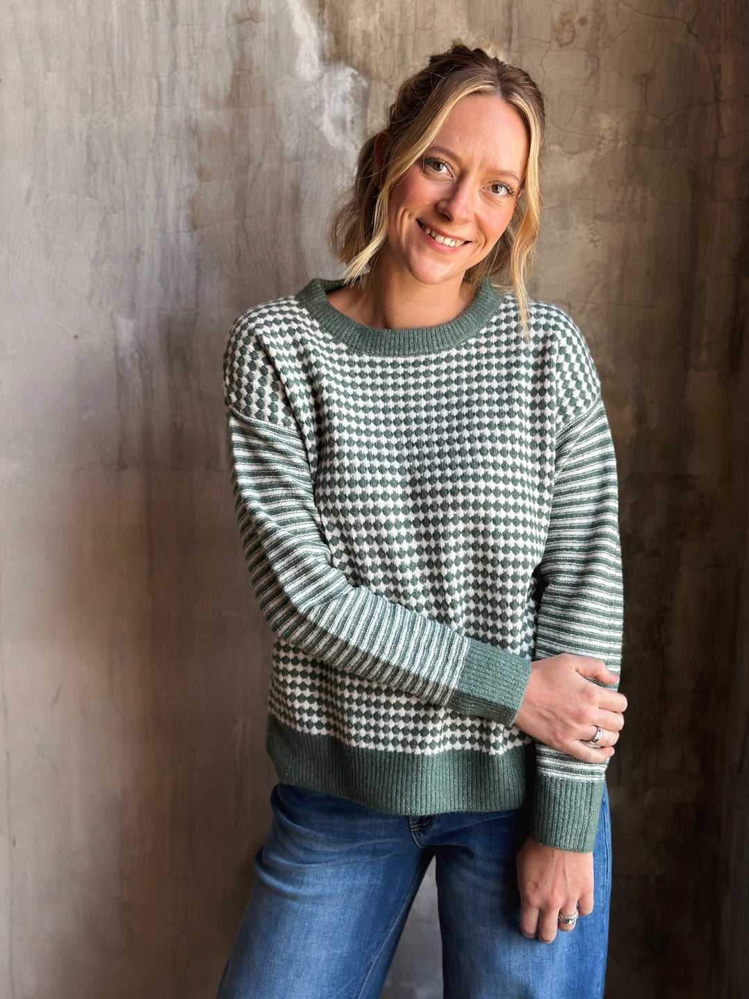 Woman wearing a green and white checkered sweater against a textured wall.