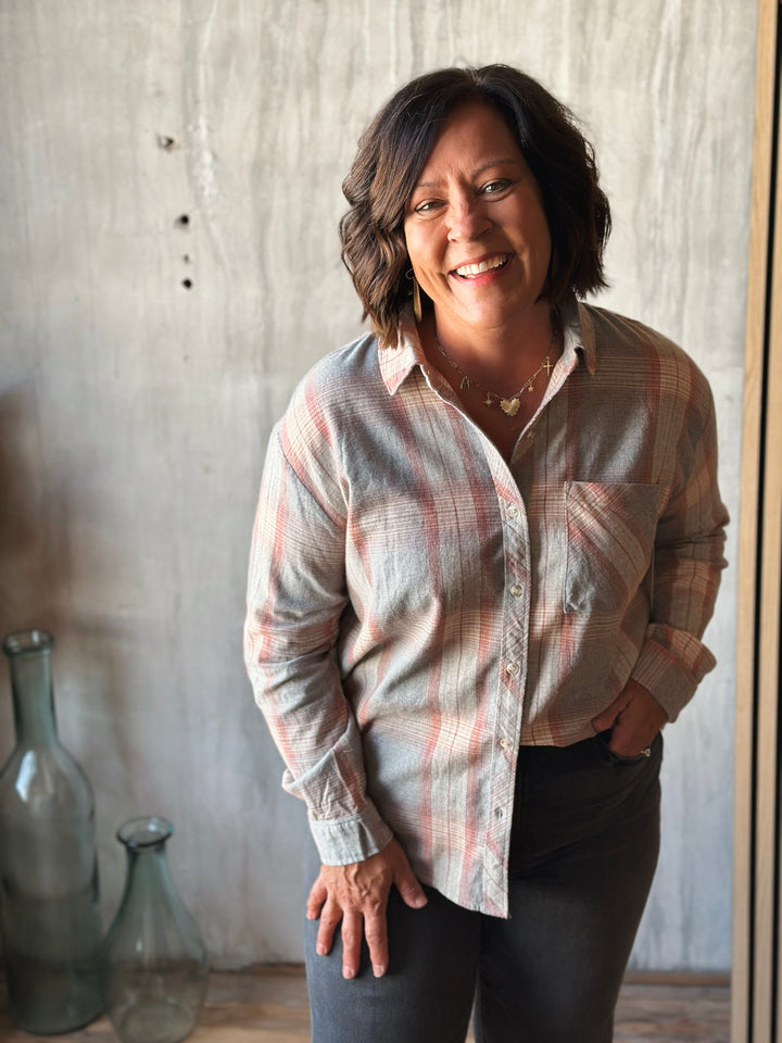 Woman wearing a plaid shirt standing in front of a textured wall with decorative bottles.