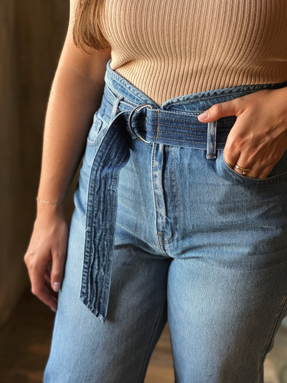 Person wearing a beige ribbed top and blue jeans with a belt.