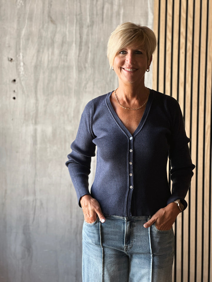 Woman wearing a blue cardigan and jeans standing against a concrete wall.