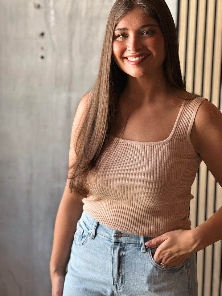 Woman wearing a beige ribbed tank top and blue jeans against a neutral background