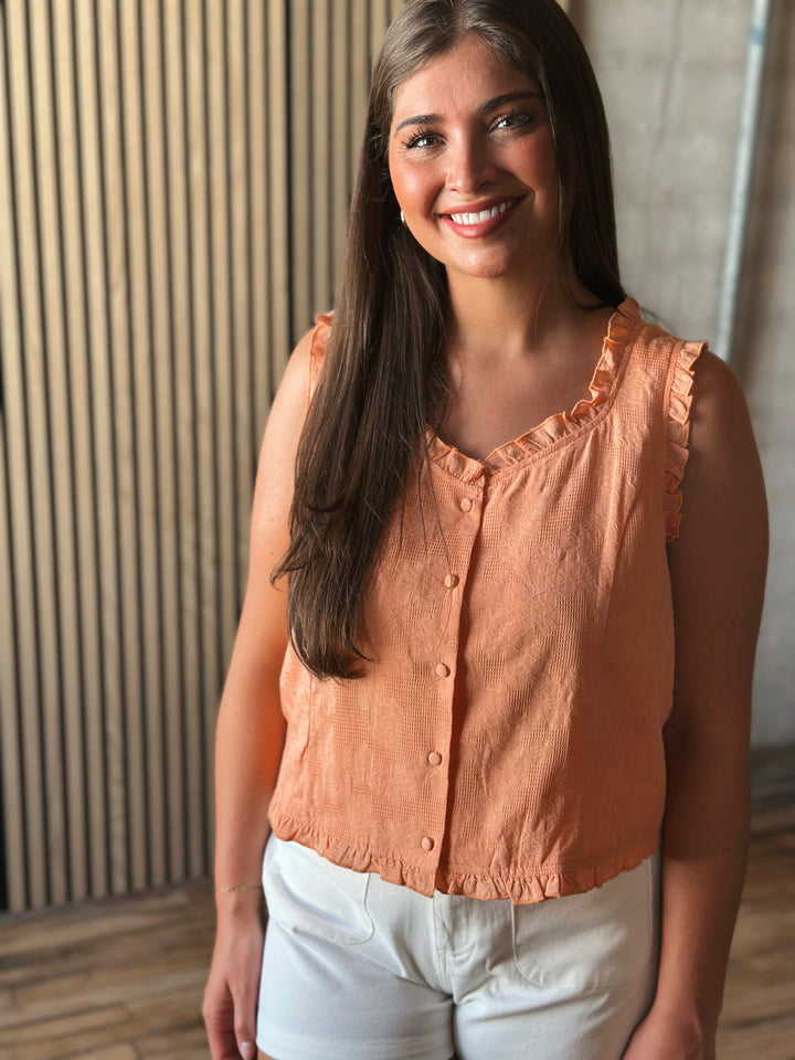 Woman wearing a peach-colored sleeveless top and white pants indoors.
