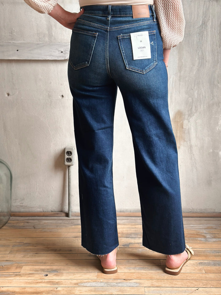 Person wearing blue jeans with a visible brand label in a minimalistic setting.