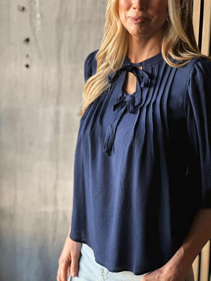 Woman wearing a navy blue blouse with ruffled details against a neutral background