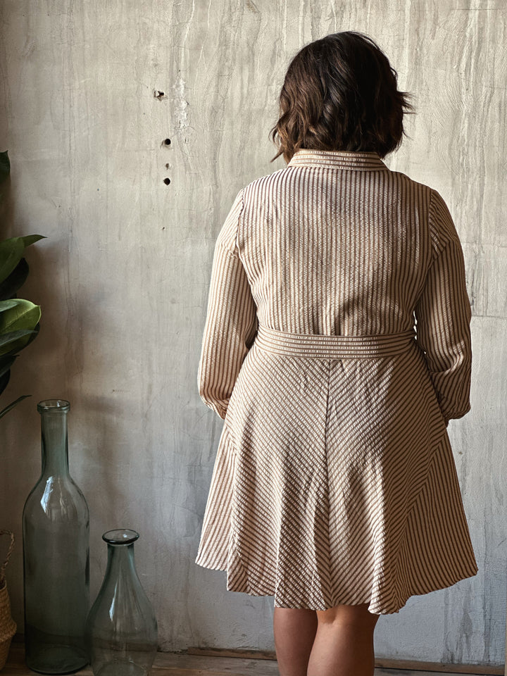 Person wearing a beige and brown striped dress against a textured wall.