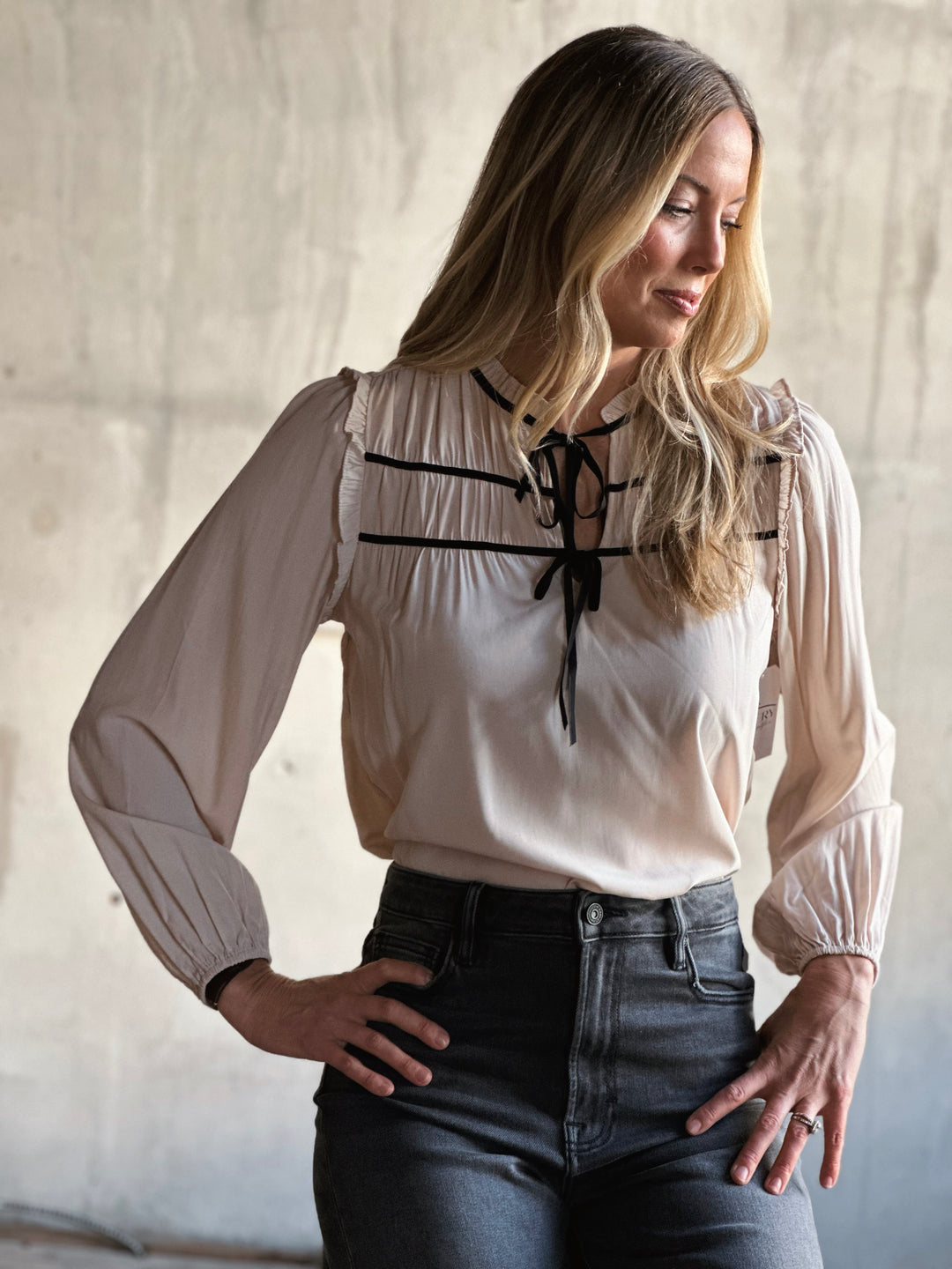 Woman wearing a white blouse with lace details and black jeans against a neutral background