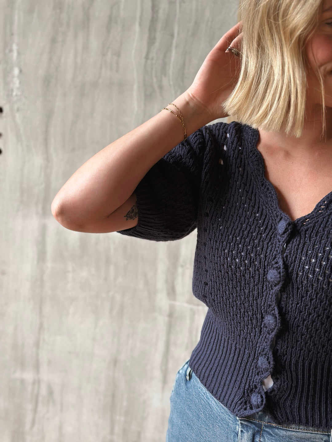 Person wearing a dark blue knitted cardigan against a light gray concrete wall.