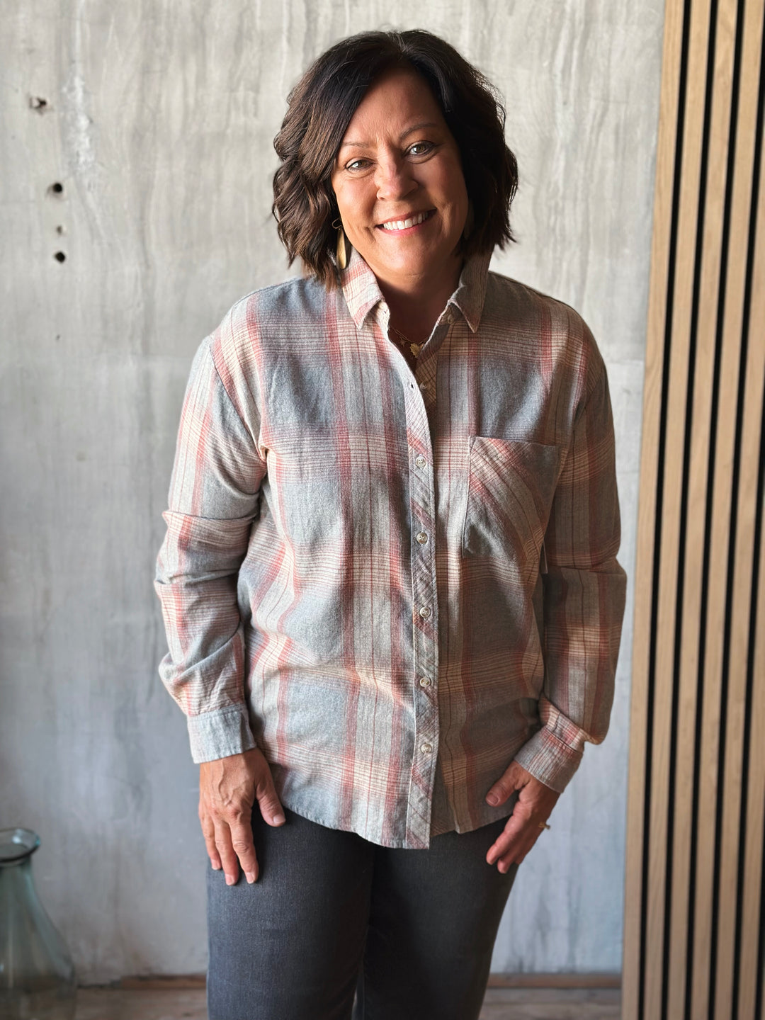 Woman wearing a plaid shirt standing against a concrete wall.