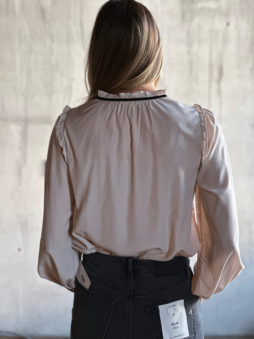 Person wearing a beige blouse with lace details in front of a neutral background