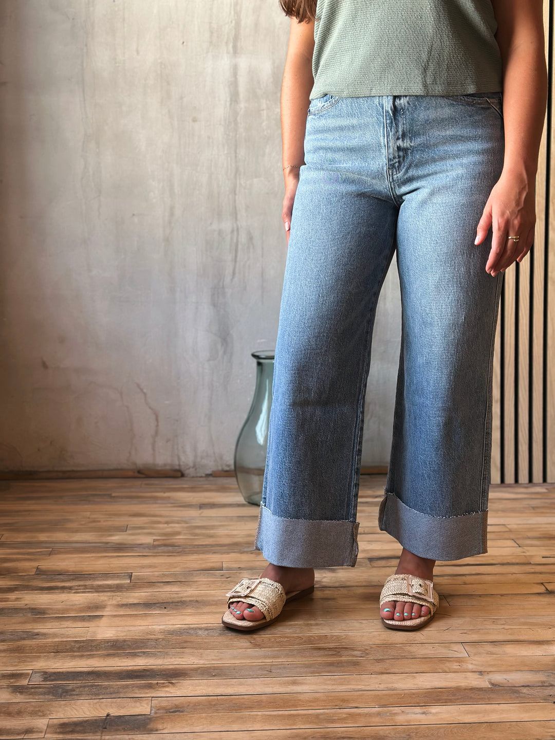 Person wearing light blue jeans standing on a wooden floor with a neutral wall background