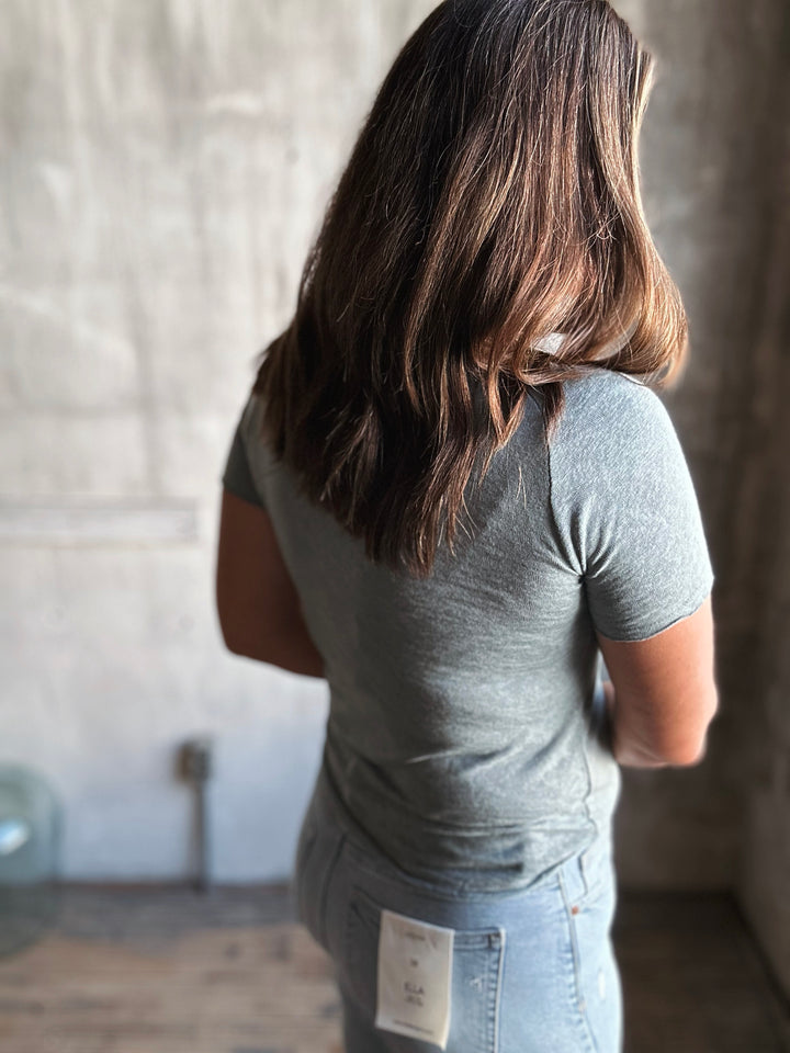 Person wearing a gray t-shirt with a visible brand label, standing against a neutral background.