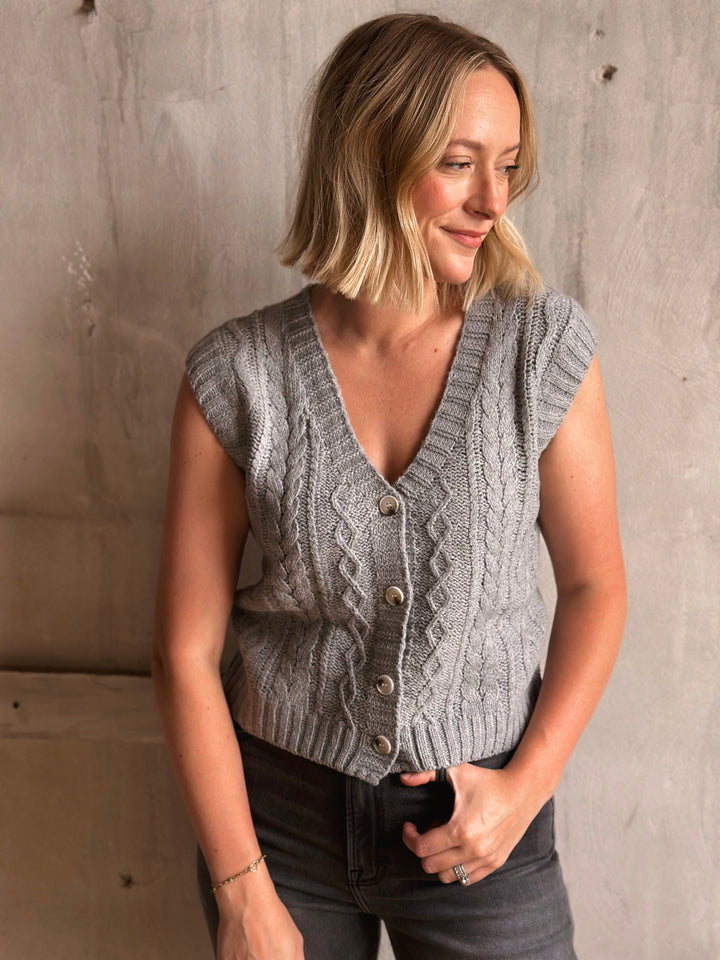 Woman wearing a gray knitted vest against a concrete wall.