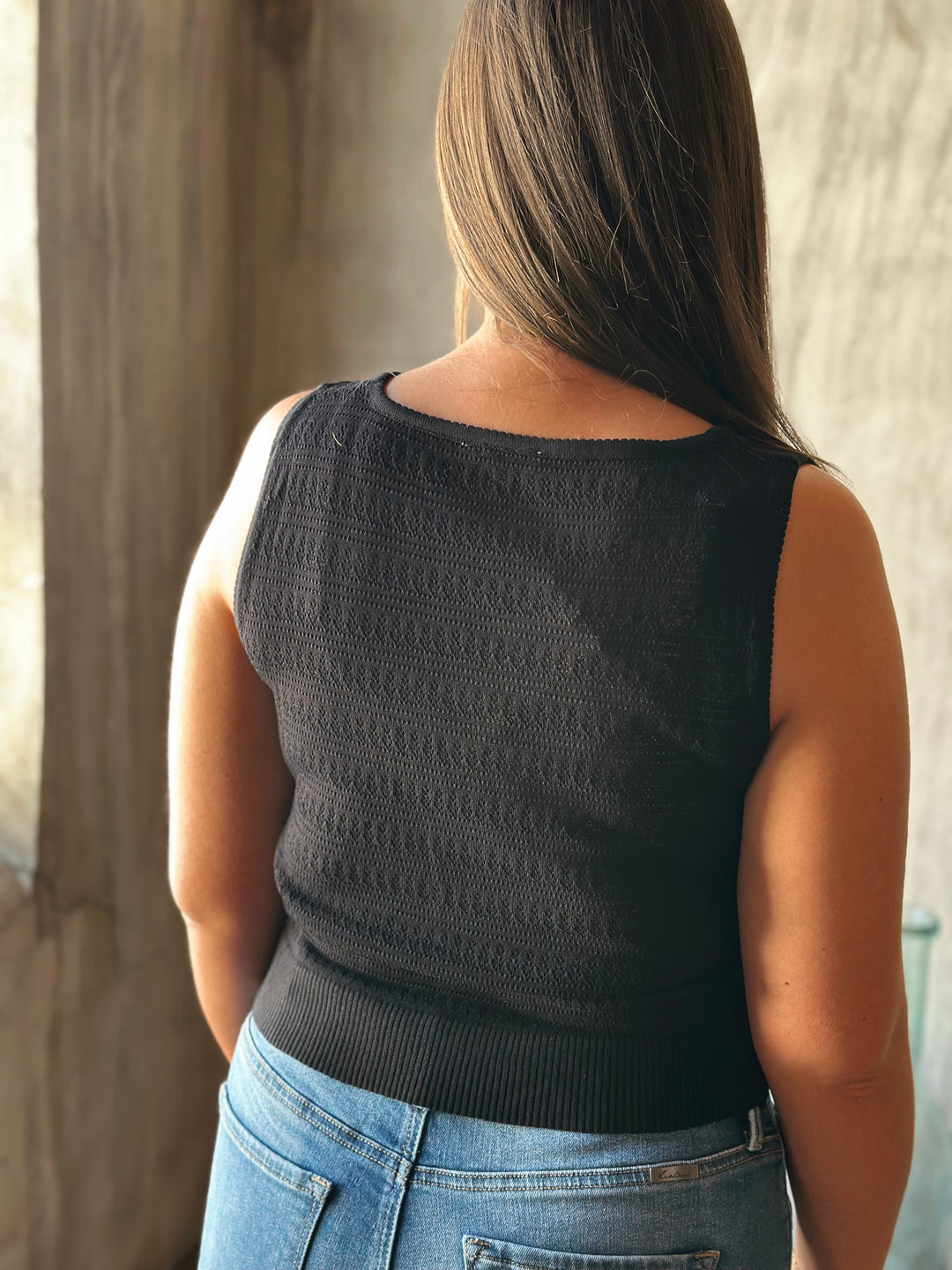 Person wearing a black sleeveless top and blue jeans, standing against a neutral background