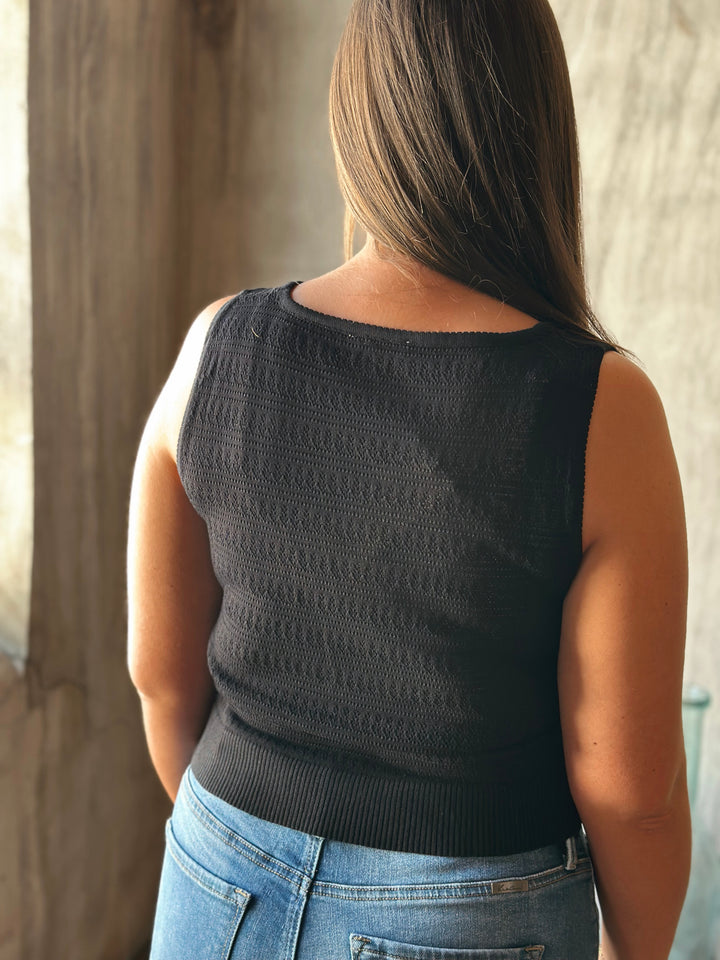 Person wearing a black sleeveless top and blue jeans, standing against a neutral background