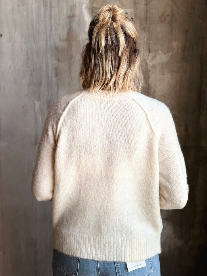 Person wearing a beige sweater against a textured wall