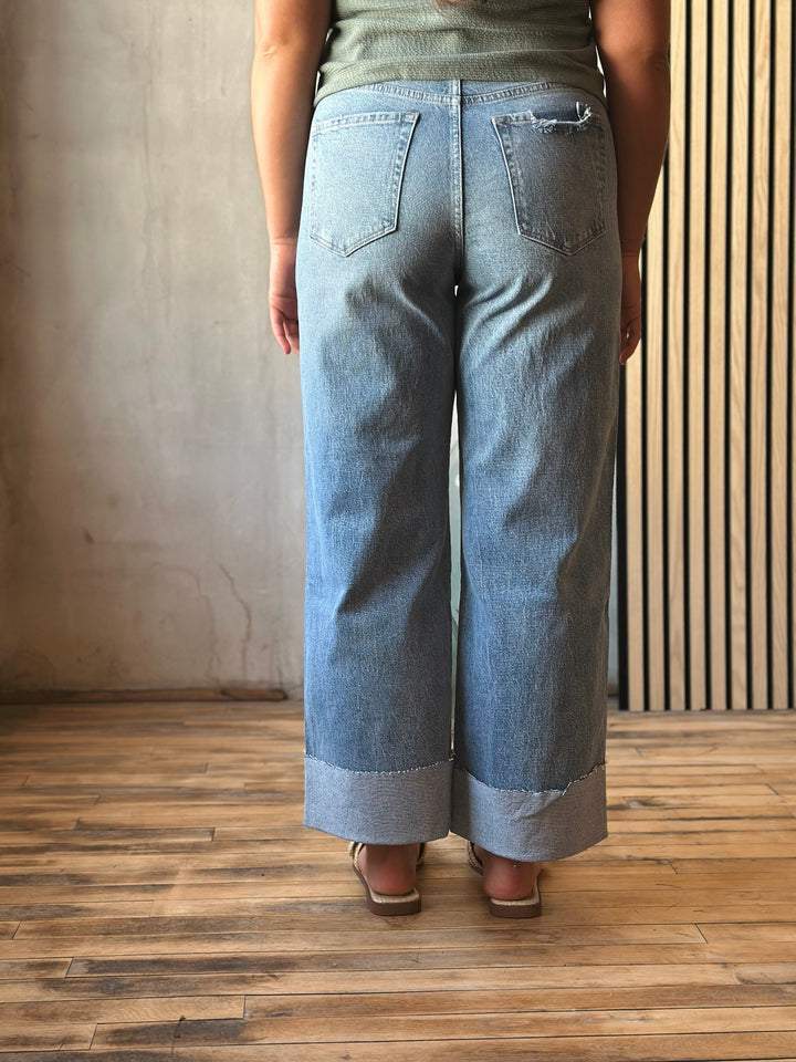 Person wearing light blue jeans standing on a wooden floor with a neutral wall background