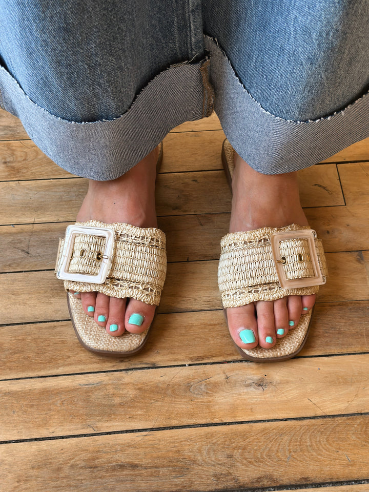 Person wearing woven sandals with a buckle on a wooden floor