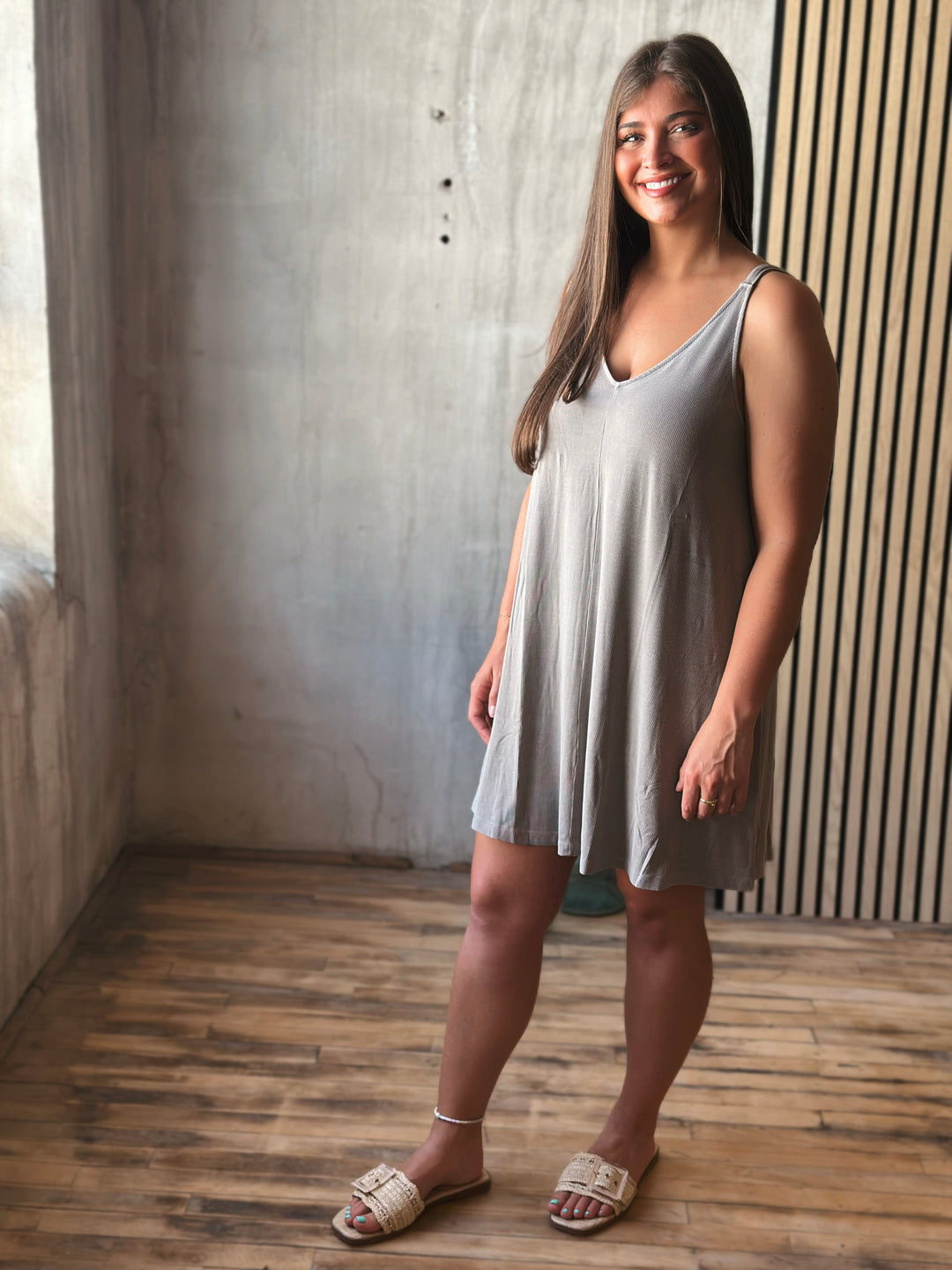 Woman wearing a light gray sleeveless dress standing against a textured wall.