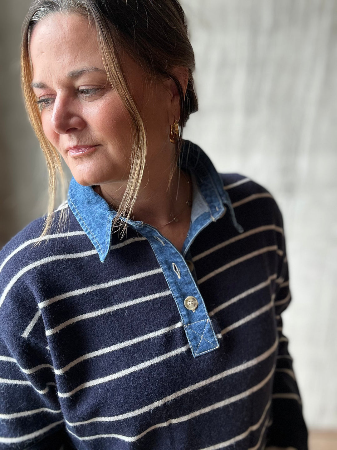 A woman wearing a navy and white striped knit sweater with a contrasting light blue denim-style collar and button placket, shown in a close-up portrait.