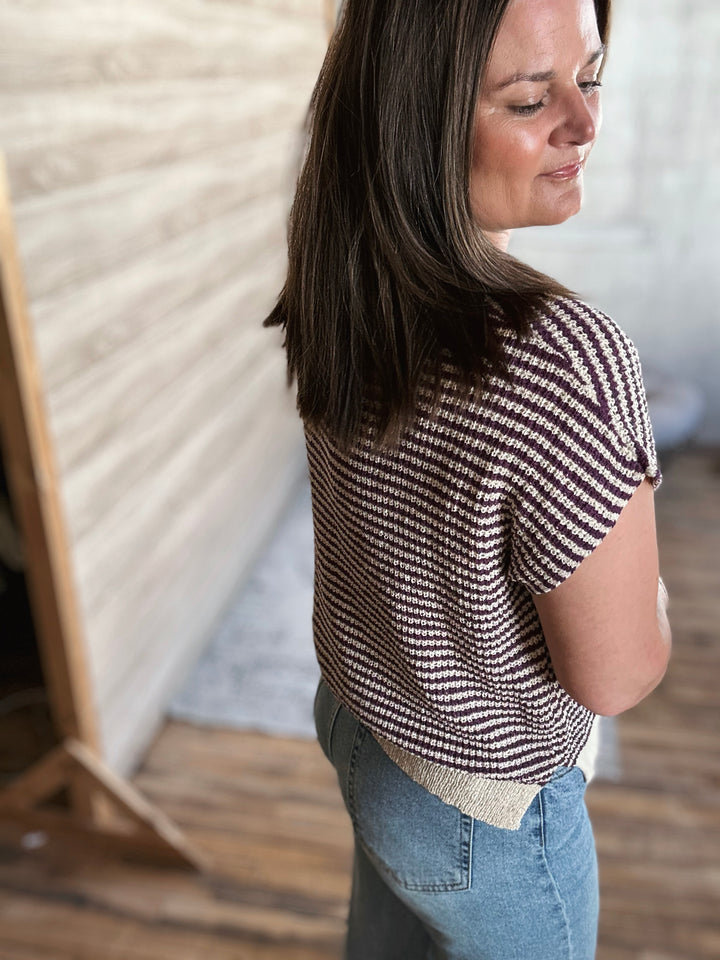 Woman wearing a beige and plum striped v-neck shirt with blue jeans, standing indoors.