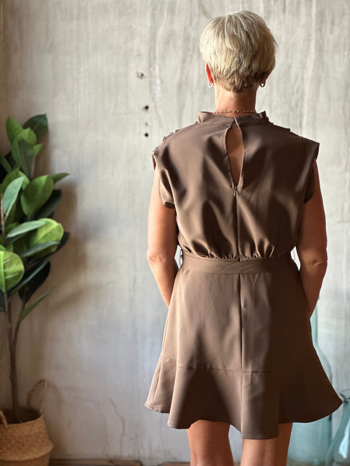 Person wearing a brown dress with a cutout back design, standing against a textured wall.