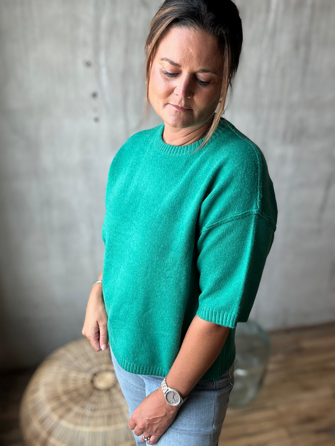 A woman wearing a vibrant green short-sleeve knit sweater and light blue jeans.