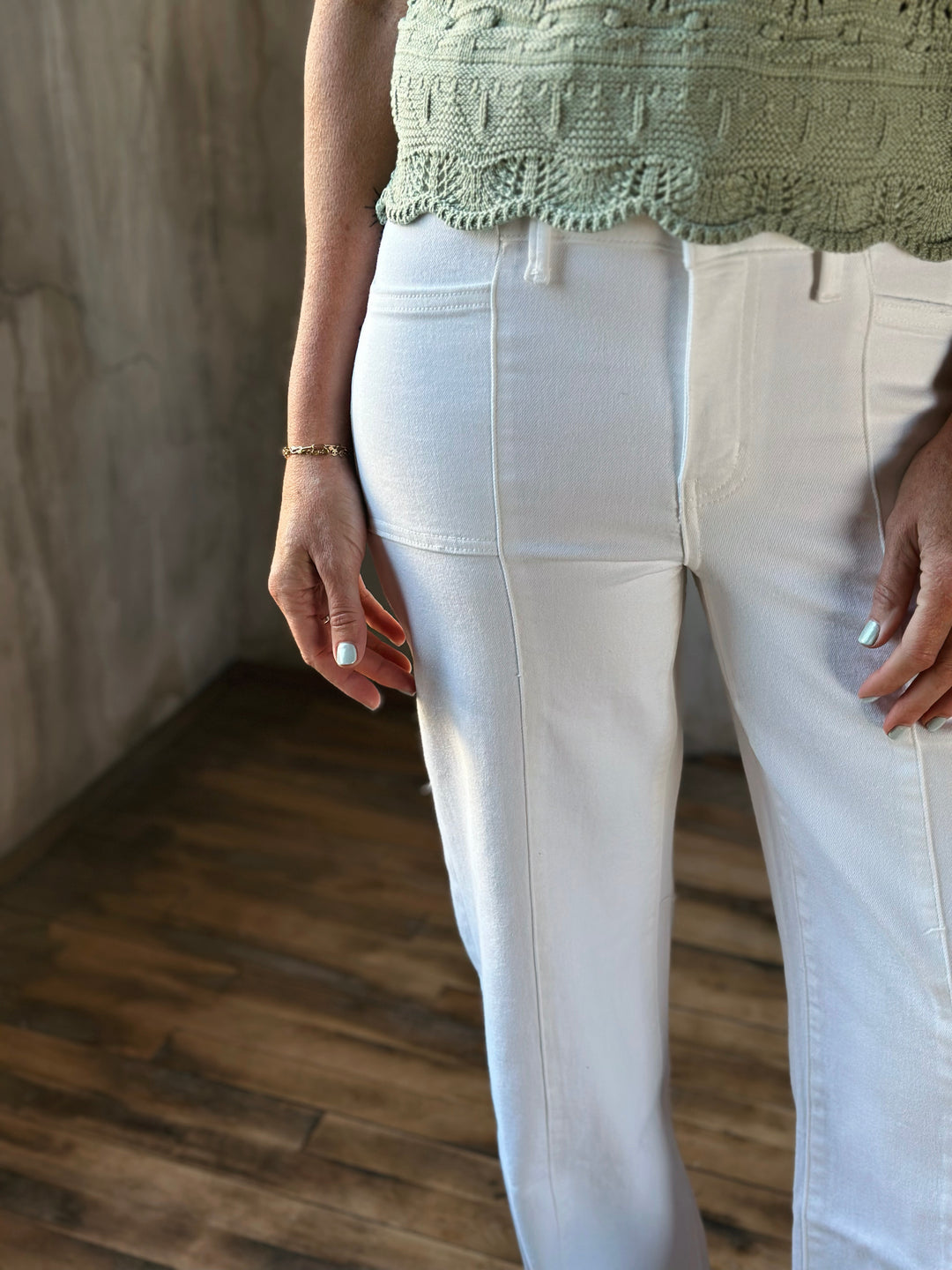Person wearing a green top and white pants in a room with wooden floor and wall.