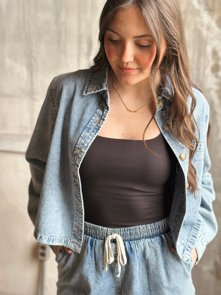 Woman wearing a denim jacket over a black top and light blue denim shorts.