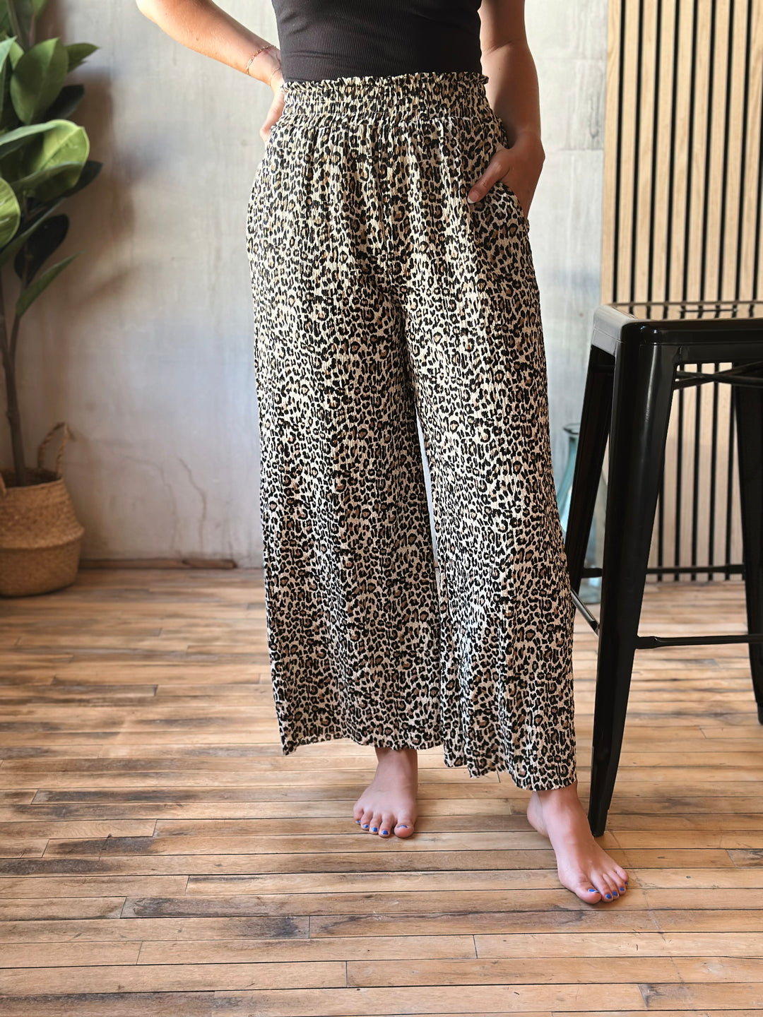 Person wearing leopard print pants standing on a wooden floor.