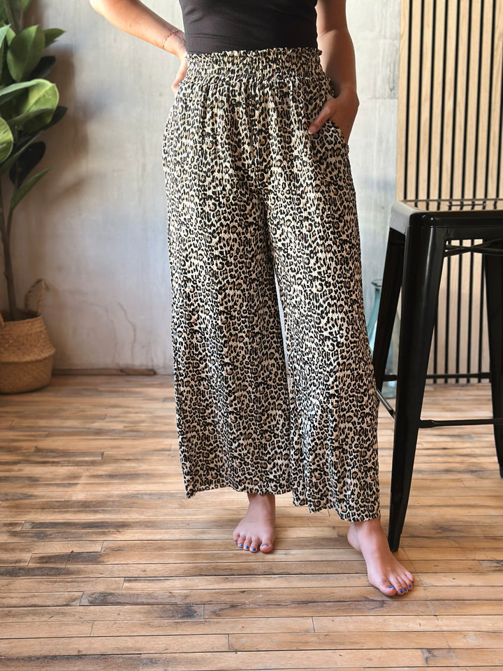 Person wearing leopard print pants standing on a wooden floor.
