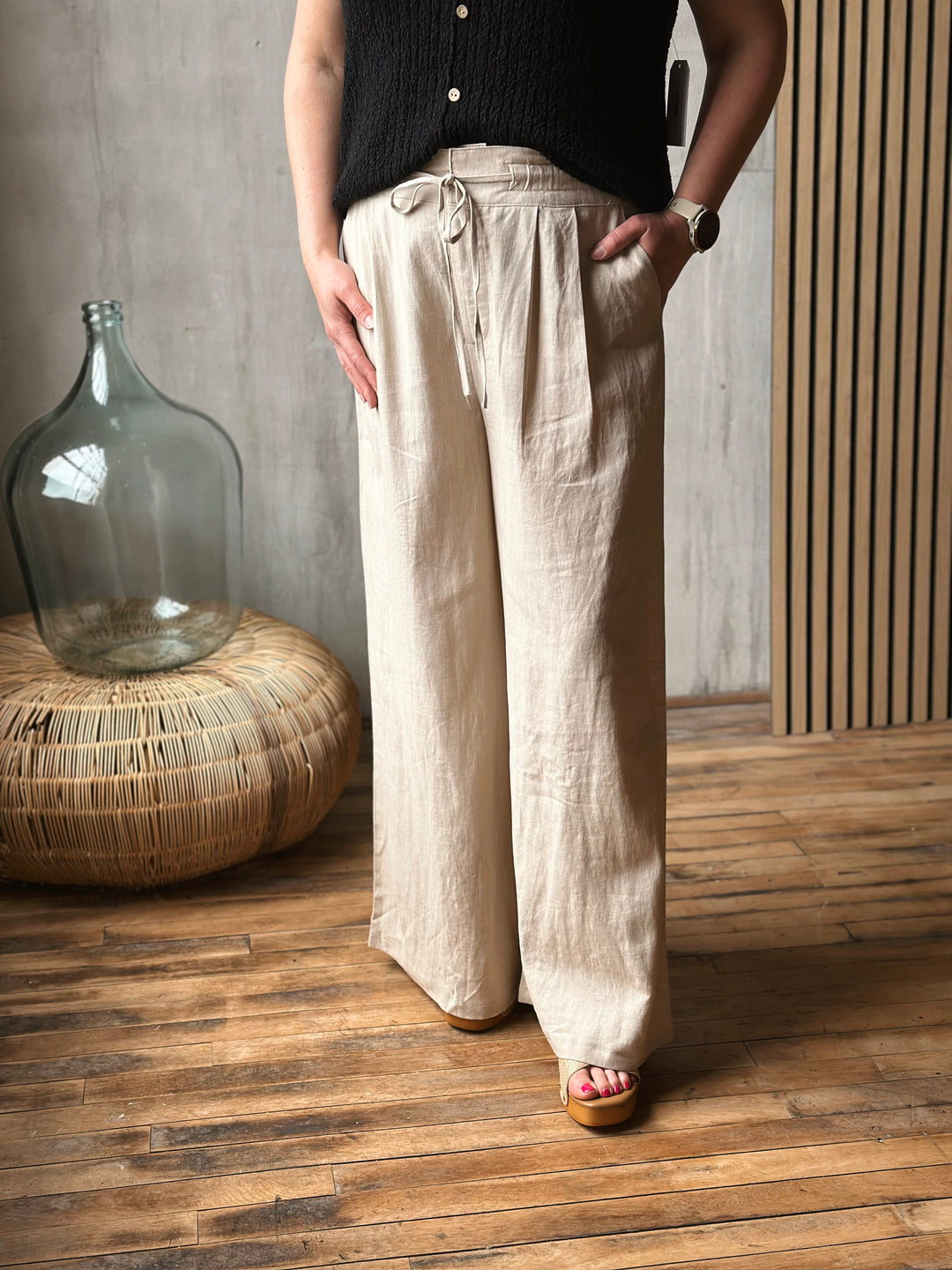 Person wearing beige wide-leg pants standing in a room with wooden flooring and a large glass container.