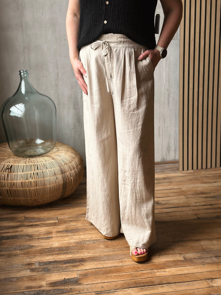 Person wearing beige wide-leg pants standing in a room with wooden flooring and a large glass container.